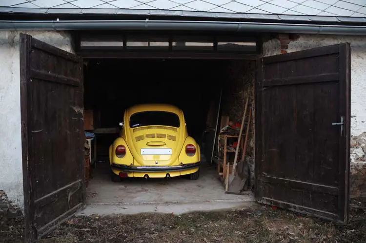 voiture coccinelle jaune stationnée dans un garage avec des portes en bois ouvertes